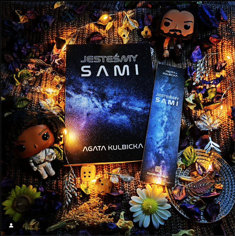 Książka "Jesteśmy sami" w otoczeniu kosmicznych gadżetów: astronauta, rakieta, neon.