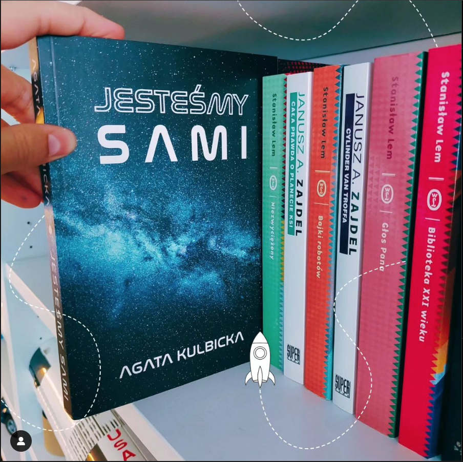 Książka "Jesteśmy sami" w otoczeniu kosmicznych gadżetów: astronauta, rakieta, neon.